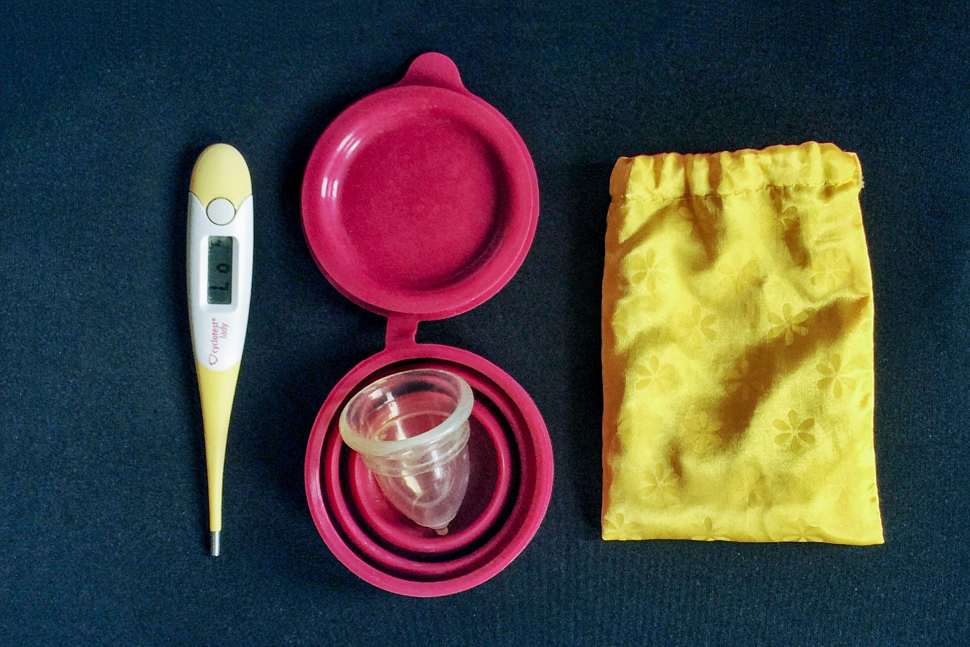 Reisehygiene: Menstruationsbecher und digitales Thermometer mit Becher und Beutel.